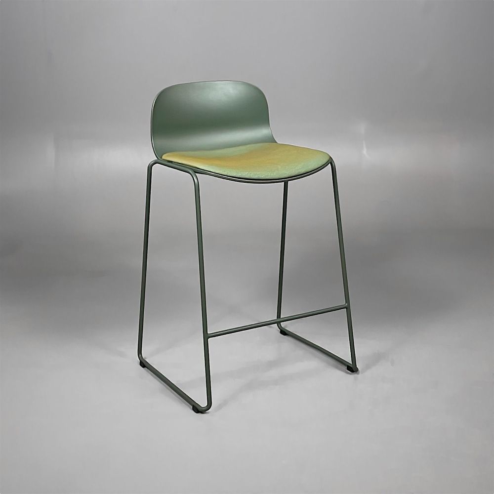 Begagnad barstol från Materia, modell Neo Lite. Stativ och skal i mörkgrön färg, helklädd sits i ett grönskimrande tyg med inslag av gult och orange. Mått: bredd 45 cm, djup 38 cm, höjd 84 cm sitthöjd 63 cm.