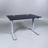 Begagnat höj- och sänkbart skrivbord med svart bordsskiva med två kabelhål, silvrigt stativ. Mått: Bredd 120 cm, Djup 80 cm, Höjd justerbar mellan 70 till 120 cm. 