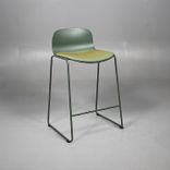 Begagnad barstol från Materia, modell Neo Lite. Stativ och skal i mörkgrön färg, helklädd sits i ett grönskimrande tyg med inslag av gult och orange. Mått: bredd 45 cm, djup 38 cm, höjd 84 cm sitthöjd 63 cm. 