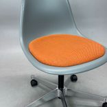 Begagnad stol med hjul Eames Plastic Side Chair PSCC från Vitra i grå plast med orange sittdyna, kromat underrede. Mått: Bredd 46,5 cm, djup 55 cm, höjd 76–88,5 cm. 