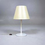 Begagnad bordslampa Melampo från Artemide i beige färg och silverstativ. Mått: Diameter 35 cm, höjd justerbar mellan 63 till 86 cm. 