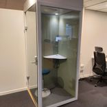 Begagnad telefonbås med vit stomme gröna innerväggar och glasdörr. Med pall och hörnbord. Mått: Bredd 100 cm, Djup 100 cm, Höjd 230 cm. 