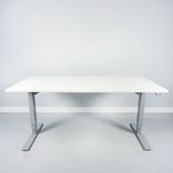 Begagnat höj och sänkbart skrivbord, med rektangulär vit bordsskiva och silvrigt stativ. Mått: Bredd: 160 cm, Djup: 80 cm, Justerbar höjd: 70–120 cm. 