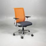 Begagnad kontorsstol från Steelcase, modell Think. Med sits i mörkgrått och rygg i orange mesh. Mått: Justerbar sitthöjd 41 till 53 cm. 