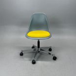 Begagnad stol med hjul Eames Plastic Side Chair PSCC från Vitra i ljusgrå plast med gul sittdyna, kromat underrede. Mått: Bredd 46,5 cm, djup 55 cm, höjd 76–88,5 cm. 