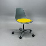 Begagnad stol med hjul Eames Plastic Side Chair PSCC från Vitra i ljusgrå plast med gul sittdyna, kromat underrede. Mått: Bredd 46,5 cm, djup 55 cm, höjd 76–88,5 cm. 