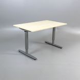 Begagnat höj-och-sänkbart skrivbord. Bordsskivan är rektangulär och gjord av björklaminat, kombinerad med ett silverstativ. Mått bredd 130 cm, djup 80 cm, Höjd 70-120 cm.